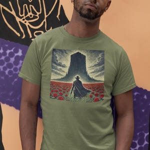 May include: A green t-shirt with a graphic print of a man in a black coat and hat walking towards a tall, dark building in a field of red flowers.