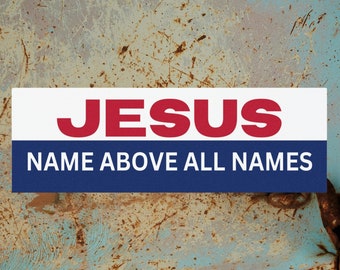 May include: A white sticker with blue and red lettering on a rusty blue metal surface. The sticker reads "JESUS NAME ABOVE ALL NAMES".