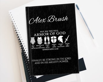 May include: Black notebook with white text that reads "Alex Brush" and "Put on the full Armour of God." The notebook features a graphic of the armour of God with the text "Ephesians 6:10" and "Finally, be strong in the Lord and in his mighty power."