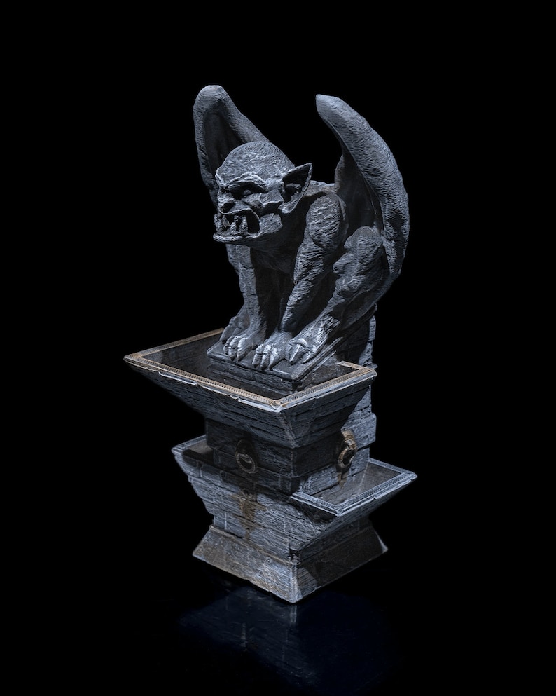 May include: A gray stone gargoyle statue with wings, perched atop a stone pedestal. The gargoyle has a fierce expression and appears to be guarding something.