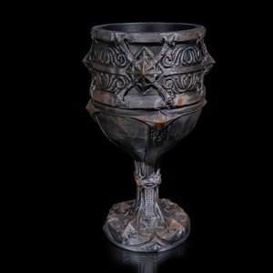 May include: A dark gray, intricately carved goblet with a wide base and a detailed design. The goblet is made of a textured material and has a medieval aesthetic.