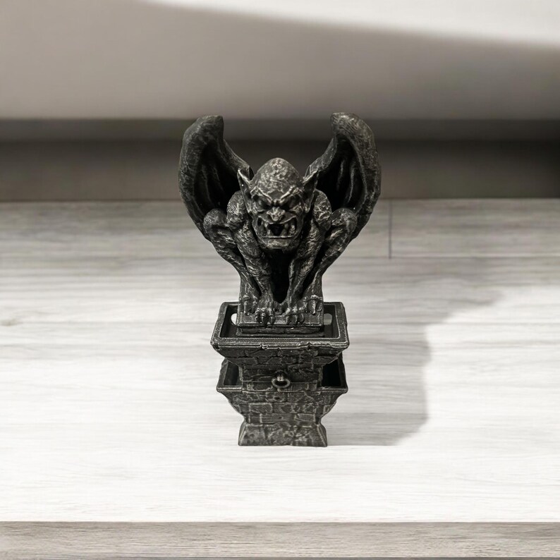 May include: A black gargoyle statue with wings perched on a stone base. The gargoyle has a menacing expression and appears to be made of a hard, durable material.