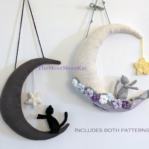May include: Two crochet moon decorations, one dark gray and one cream-colored, each with a crocheted cat and star. The dark gray moon has a black cat, and the cream moon has a gray cat. The cream moon is decorated with flowers.