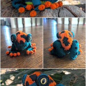 May include: A crocheted frog figurine featuring a vibrant color palette of orange, teal, and black. The frog has large, prominent yellow eyes with black pupils, textured skin, and small orange toes. The body displays a patterned design.