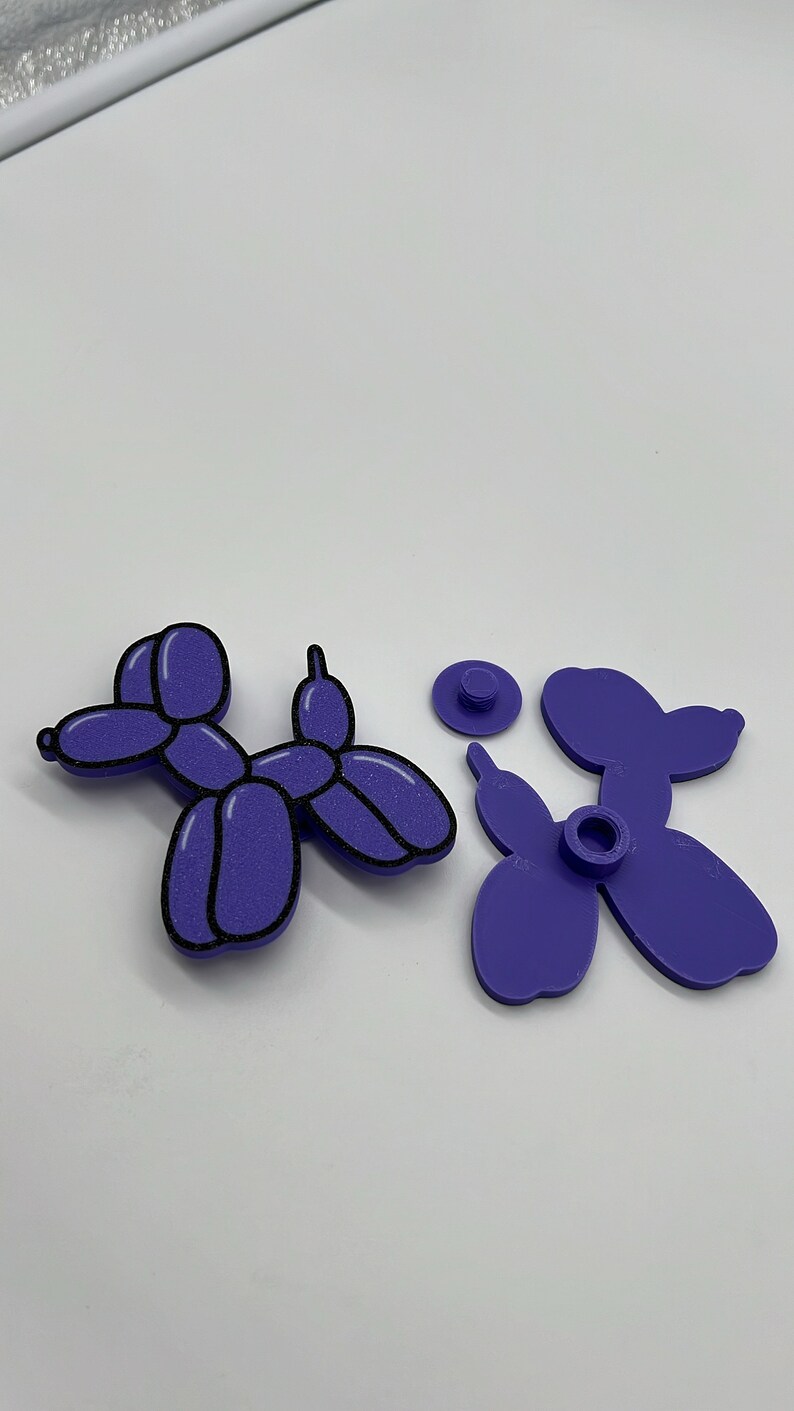 Pode incluir: Um animal de bal&atilde;o roxo em forma de c&atilde;o, desmontado em tr&ecirc;s pe&ccedil;as. O c&atilde;o &eacute; feito de um material texturizado e tem um contorno preto.