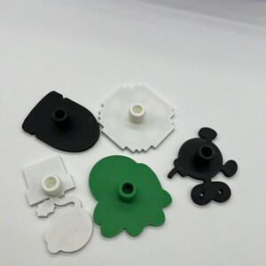 Puede incluir: Una colecci&oacute;n de cortadores de galletas de pl&aacute;stico de colores en varias formas, incluyendo un Mickey Mouse negro, una mancha verde y un copo de nieve blanco. Cada cortador tiene un poste central.
