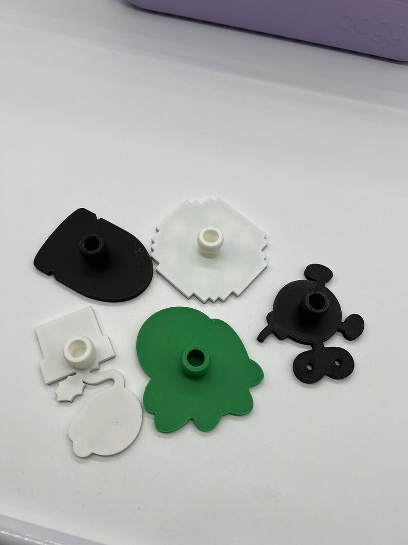 Puede incluir: Una colecci&oacute;n de cortadores de galletas de pl&aacute;stico de colores en varias formas, incluyendo un Mickey Mouse negro, una mancha verde y un copo de nieve blanco. Cada cortador tiene un poste central.
