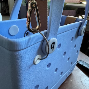 May include: A light blue tote bag with a brown strap and a gold clasp. The bag has a number "9" on the side and a white button.