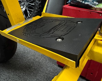 Puede incluir: Un marco de metal amarillo con un reposapiés de goma negra. El reposapiés tiene un diseño en relieve de un camión. El marco tiene una manguera negra unida a él.