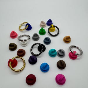 Może przedstawiać: Zestaw kolorowych plastikowych pierścieni i podstaw. Pierścienie są wykonane z metalu i dostępne są w kolorze złotym, srebrnym i czarnym. Podstawy są wykonane z plastiku i dostępne są w różnych kolorach, w tym czerwonym, niebieskim, zielonym, żółtym i fioletowym.