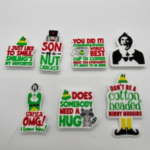 May include: Seven colourful rectangular pins with quotes and characters from the film "Elf." The pins feature phrases such as "I just like to smile" and "Does somebody need a hug?" with images of Buddy the Elf and a raccoon.