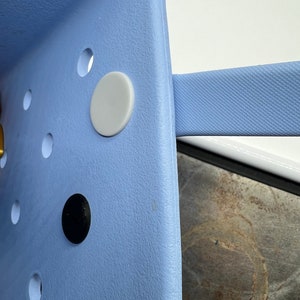 Pode incluir: Um close-up de uma cadeira de pl&aacute;stico azul claro com um bot&atilde;o branco e um bot&atilde;o preto. A cadeira tem uma superf&iacute;cie texturizada.