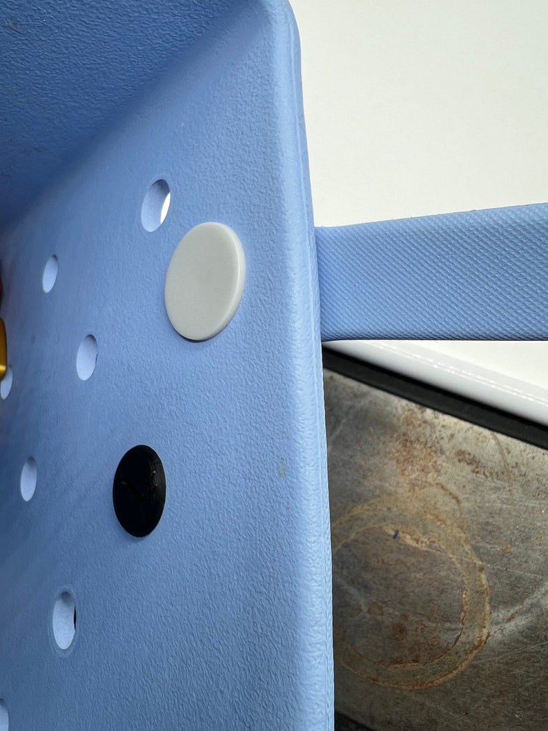 Pode incluir: Um close-up de uma cadeira de pl&aacute;stico azul claro com um bot&atilde;o branco e um bot&atilde;o preto. A cadeira tem uma superf&iacute;cie texturizada.