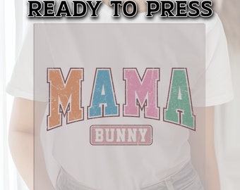 May include: A white t-shirt with a vintage-style graphic that says "MAMA BUNNY" in colorful letters with a distressed look.
