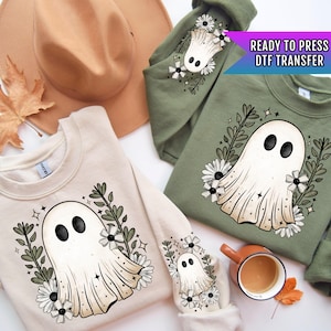 May include: Two cream colored sweatshirts with a white ghost design with black eyes and a floral pattern. The text "READY TO PRESS DTF TRANSFER" is on a green sweatshirt.