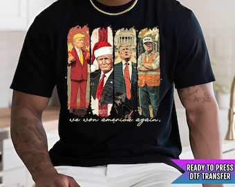 Puede incluir: Una camiseta negra con un estampado gráfico de cuatro hombres en un diseño navideño. El texto "We won America again." está impreso debajo del gráfico. La camiseta es una transferencia DTF lista para presionar.