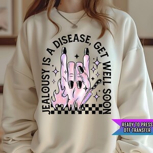 May include: A white sweatshirt with a black and pink graphic design that says "Jealousy is a disease, get well soon". The graphic features a hand making the rock and roll sign with flames and a knife.
