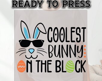 May include: A white t-shirt with a black and white graphic of a bunny wearing sunglasses and the text "Coolest Bunny on the Block". The graphic also includes a blue and orange Easter egg.