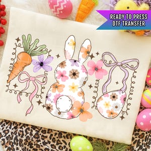 May include: A cream-colored DTF transfer featuring a floral bunny, carrot, and Easter egg design. The bunny is filled with colorful flowers. The design includes a carrot, flowers, and a purse-shaped egg. Text reads "READY TO PRESS DTF TRANSFER".
