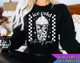 Puede incluir: Sudadera negra con un gráfico blanco de una copa de helado llena de calaveras con el texto "ice cold like my soul" y un fondo a cuadros. Transferencia DTF lista para presionar.