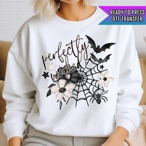 May include: White sweatshirt with a black and white graphic design that says "perfectly wicked" with a spider web, flowers, and bats.