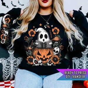May include: A black sweatshirt with a graphic print of a ghost reading a book inside a jack-o'-lantern. The ghost is surrounded by flowers, mushrooms, and a bee. The text "READY TO PRESS DTF TRANSFER" is at the bottom of the image.