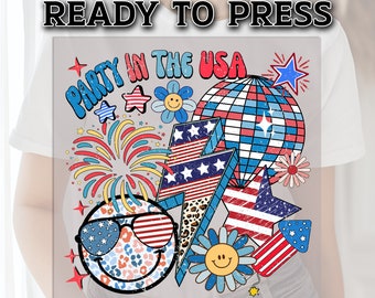 May include: A sublimation design featuring a smiley face wearing sunglasses with red, white, and blue stars and stripes. The design also includes fireworks, a disco ball, a lightning bolt, and flowers. The text "Party in the USA" is written in a retro font.