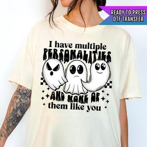May include: A white t-shirt with a black graphic of three ghosts. The text on the shirt reads "I have multiple personalities and none of them like you".