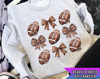 May include: Gray sweatshirt with a design of brown footballs and brown bows. The text "READY TO PRESS DTF TRANSFER" is at the bottom of the image.