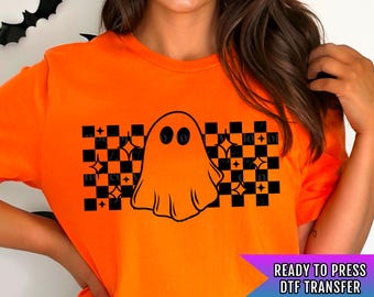 May include: Orange t-shirt with a black and white checkered pattern and a ghost graphic. The text "READY TO PRESS DTF TRANSFER" is on the bottom right corner of the image.