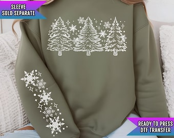 May include: A green sweatshirt with a white design of three stylized Christmas trees and snowflakes. The text "READY TO PRESS DTF TRANSFER" is on the bottom right corner of the sweatshirt. The text "SLEEVE SOLD SEPARATE" is on the top left corner of the sweatshirt.