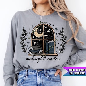May include: A gray long-sleeve shirt with a graphic of a window with a crescent moon and stars, a stack of books, and the text "midnight reader".