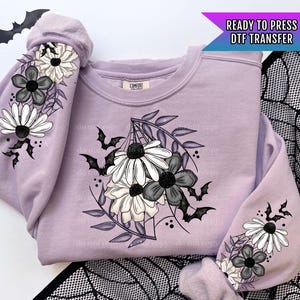 May include: Purple sweatshirt with a black and white floral design featuring bats and spiderwebs. The design is on the front and sleeves of the sweatshirt. "READY TO PRESS DTF TRANSFER" is written in the top right corner of the image.