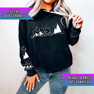 May include: Black hoodie with a white graphic design of a mountain range, sun, moon, and trees. The text "READY TO PRESS DTF TRANSFER" is on the bottom right corner of the image. "SLEEVE SOLD SEPARATE" is on the top left corner of the image.