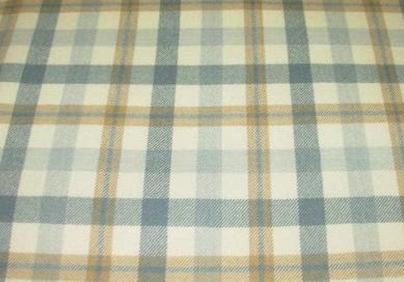 May include: A woven fabric featuring a plaid pattern with intersecting lines in shades of light blue, tan, and cream. The textile displays a consistent grid design with alternating vertical and horizontal stripes that create a classic checkered appearance.