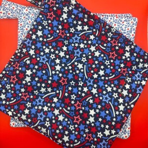 Puede incluir: Dos agarraderas de olla con estampado rojo, blanco y azul. La agarradera superior tiene un estampado de estrellas y rayas rojas, blancas y azules. La agarradera inferior tiene un estampado de flores blancas sobre un fondo azul.