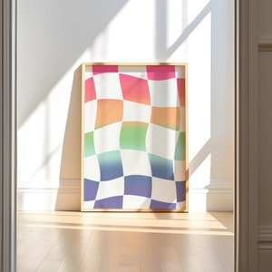 Könnte beinhalten: Ein gerahmter Kunstdruck mit einem farbenfrohen, wellenförmigen Schachbrettmuster in Rosa, Orange, Grün, Blau und Lila. Das Kunstwerk wird in einem Raum mit Holzboden und weißen Wänden mit Sonneneinstrahlung gezeigt.