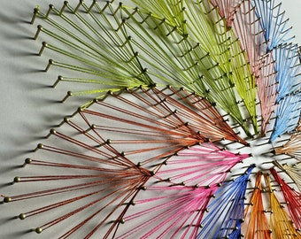 May include: A colourful string art piece with a circular design. The strings are arranged in a radial pattern, creating a starburst effect. The colours of the strings include red, orange, yellow, green, blue, and purple.
