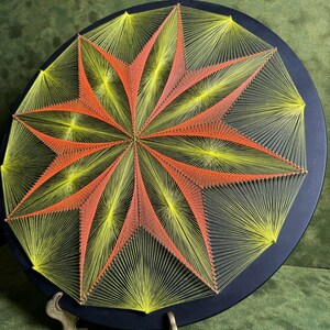 May include: A circular string art piece with a geometric design. The design is made with yellow and orange string on a black background.