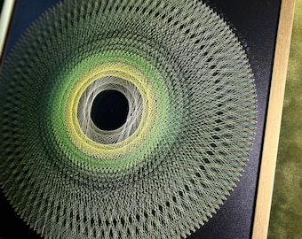 May include: A framed circular string art piece with a black background. The string art is made with green and yellow thread, creating a concentric circle pattern.