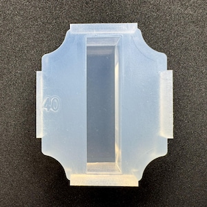 Könnte beinhalten: Eine transparente, rechteckige Silikonform mit einem zentralen, vertieften Bereich und dekorativen Kanten. Die Zahl "40" ist auf der Seite sichtbar. Die Form ist für die Herstellung und das Gießen konzipiert.