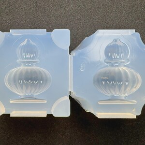 May include: Two-part, pale blue silicone mould for creating a decorative perfume bottle. The mould features a detailed design of a vintage-style bottle with a ribbed body and a decorative stopper. Suitable for resin casting or soap making.