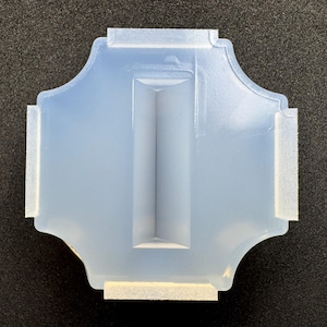 May include: A light blue, ornate-shaped silicone mold with a central rectangular channel and white foam pads attached to the edges. The mold is designed for crafting and casting projects.