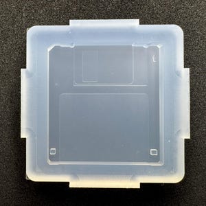 May include: A translucent, square silicone mold featuring the embossed shape of a classic 3.5-inch floppy disk. The mold has a smooth, matte finish with raised edges and distinct rectangular and square indentations that replicate the iconic design.