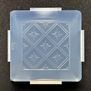 May include: A square, translucent silicone mold featuring a repeating diamond pattern with embossed star shapes in the center of each diamond. The mold has small tabs on each side and the letter B is embossed on the left edge of the frame.