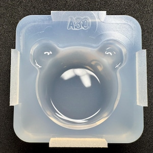 Peut inclure: Un moule en silicone carré et translucide présentant une cavité centrale en forme d'ours. Le moule possède des coins arrondis et le texte A30 est gravé sur le bord supérieur. Le matériau est semi-transparent avec une finition lisse et souple.