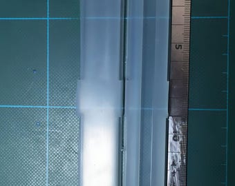 May include: Two translucent, rectangular molds, each approximately 5 inches long, are displayed against a green grid background. A ruler is placed next to the molds for scale. The molds have a rectangular shape with rounded ends and a central cavity.