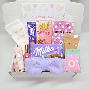May include: A gift box labeled The Preppy Teen containing white socks with pink hearts, Cadbury hot chocolate, strawberry Pocky, a Bubble T sheet mask, a star bracelet, Milka Oreo chocolate, a lavender bow headband, hand cream, and bath salts.