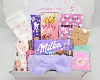 May include: A gift box labeled The Preppy Teen containing white socks with pink hearts, Cadbury hot chocolate, strawberry Pocky, a Bubble T sheet mask, a star bracelet, Milka Oreo chocolate, a lavender bow headband, hand cream, and bath salts.