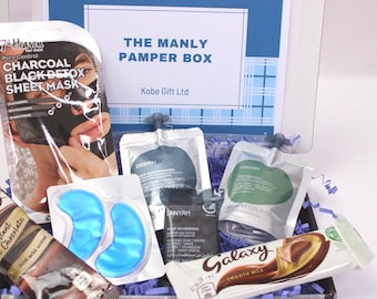 May include: A gift box labeled "THE MANLY PAMPER BOX" contains skincare products, including a charcoal sheet mask, eye patches, and various lotions. A Galaxy chocolate bar and a tube of instant hot chocolate are also included. The box is decorated with blue and white accents.